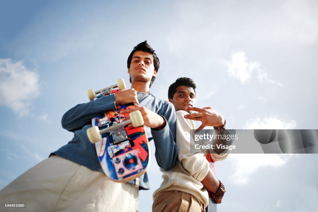 Low angle view of two young men standing with a skate board