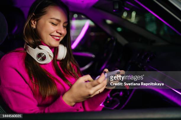 girl in headphones plays on a smartphone in the car at night - music from the motor city stock pictures, royalty-free photos & images