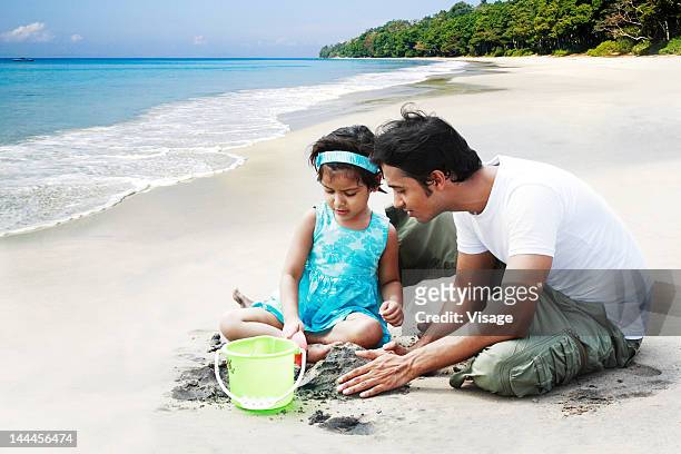 baby girl with her father playing with sand at a beach - asian father and daughter stock pictures, royalty-free photos & images