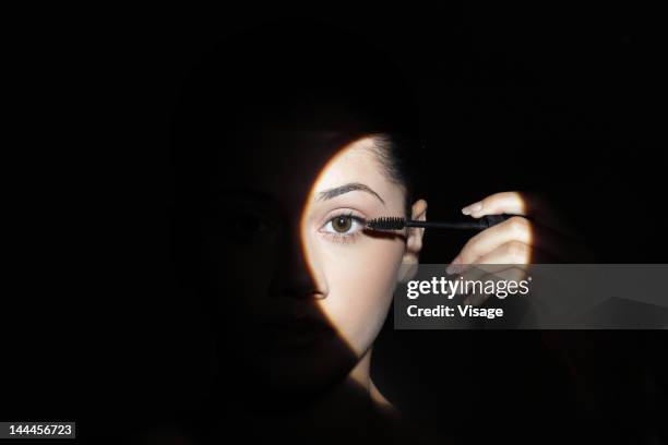 young woman applying mascara to her lashes - woman spotlight stock pictures, royalty-free photos & images