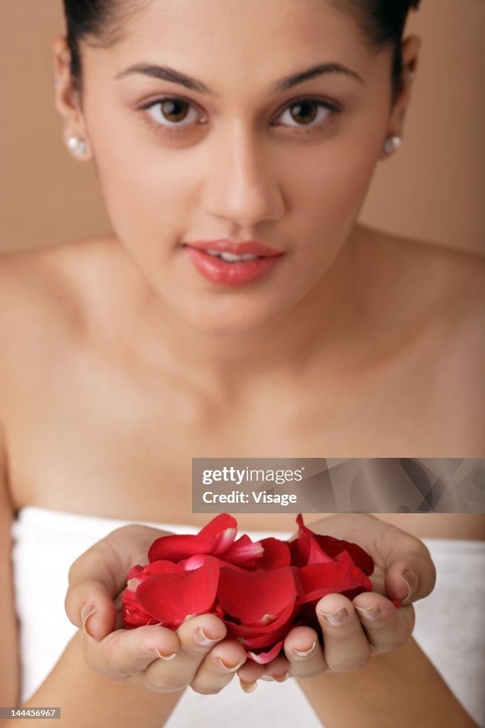 Young woman wrapped in towel holding rose petals