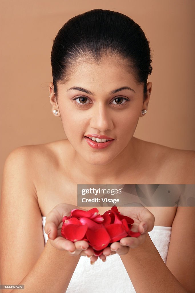 Young woman wrapped in towel holding rose petals