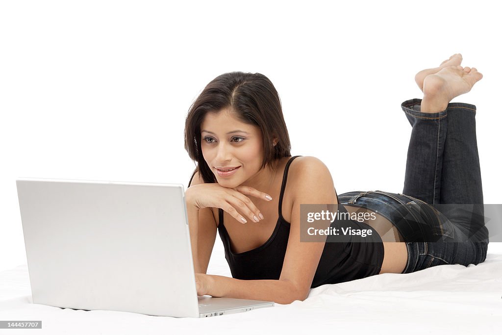 Young woman working on a laptop lying in bed