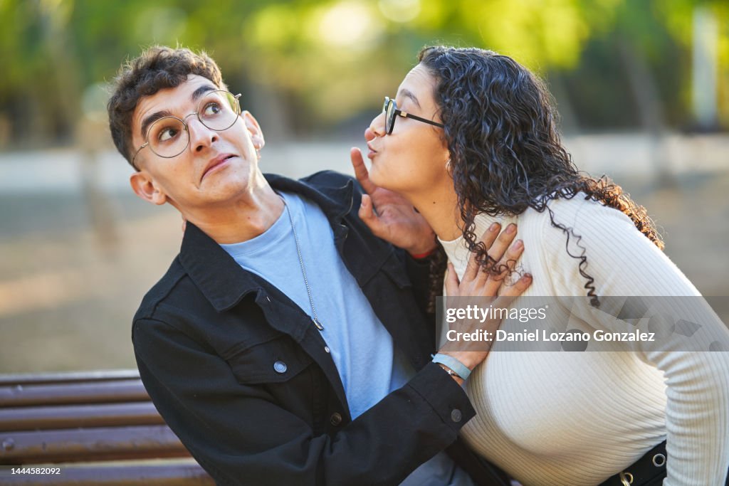 Man rejecting a woman while she tries to kiss him during a date in a park.