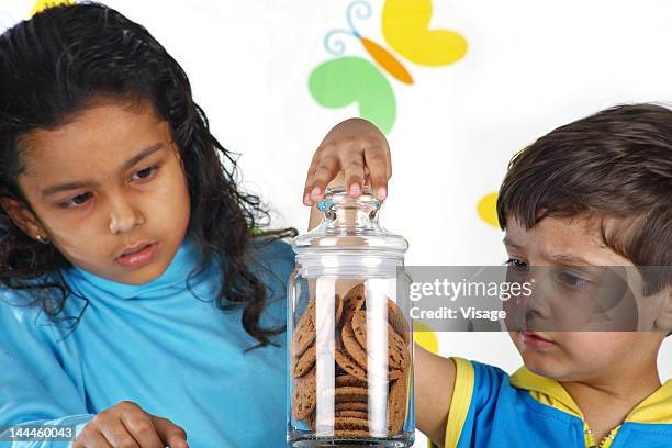 girl and boy trying to open a jar of cookies - cookie jar stock pictures, royalty-free photos & images