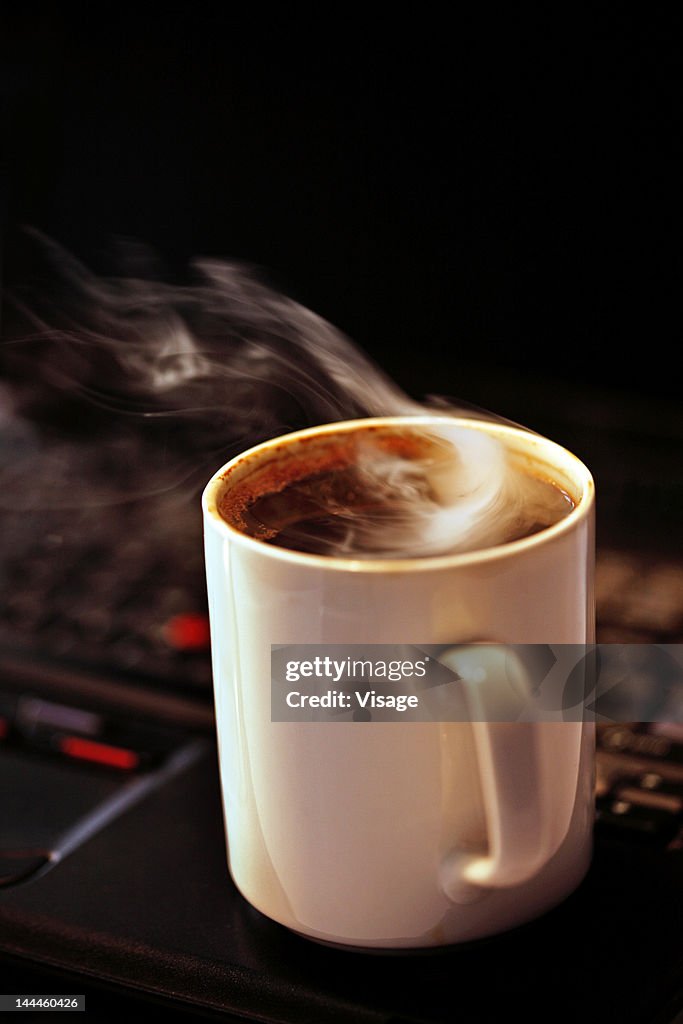 Close up of a steaming coffee mug on a laptop
