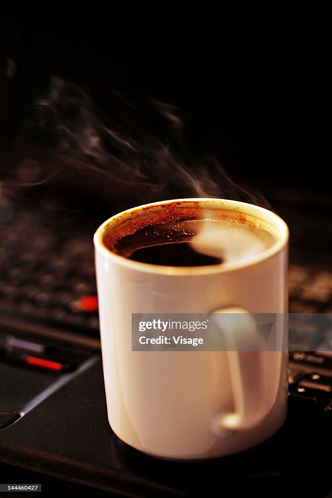 Close up of a steaming coffee mug on a laptop