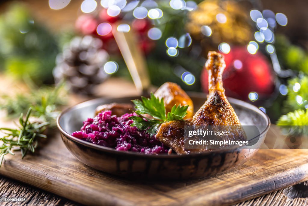 Duck or goose leg served with red cabbage and baked potatoes in a retro pan on a festive Christmas decorated table.