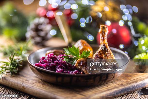 duck or goose leg served with red cabbage and baked potatoes in a retro pan on a festive christmas decorated table. - duck stock pictures, royalty-free photos & images