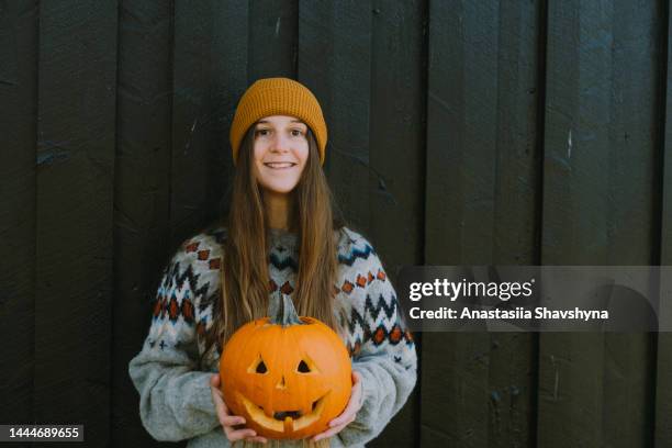 eine frau in wollpullover, die jack o'lantern kürbis hält, bleibt am schwarzen holzhintergrund - traditionally norwegian stock-fotos und bilder