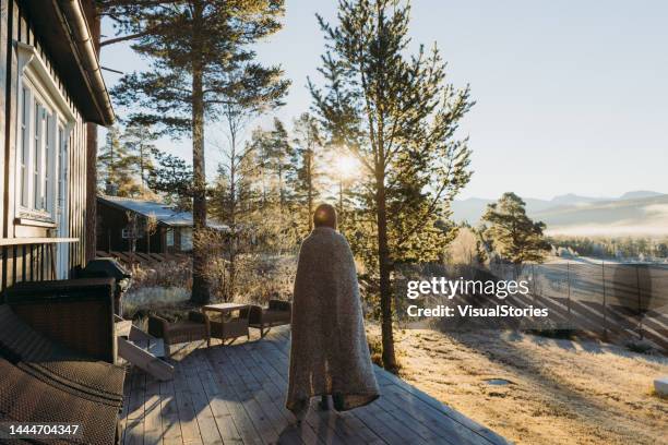 weibchen beim sonnenaufgang über die berge von der hausterrasse im wald in norwegen - hütte stock-fotos und bilder