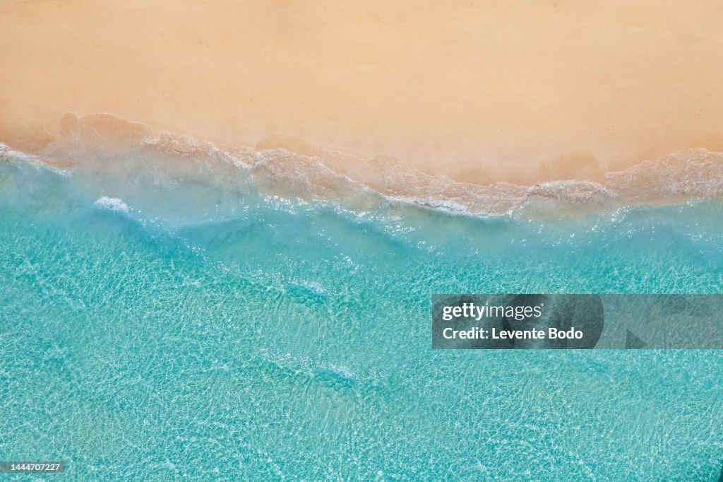 Summer seascape beautiful waves, blue sea water in sunny day. Top view from drone. Sea aerial view, amazing tropical nature background. Beautiful bright sea waves splashing and beach sand sunset light