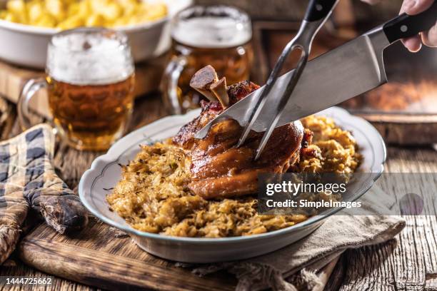 the cook's hands cut the freshly baked bavarian knee with sauerkraut. - chispes - fotografias e filmes do acervo