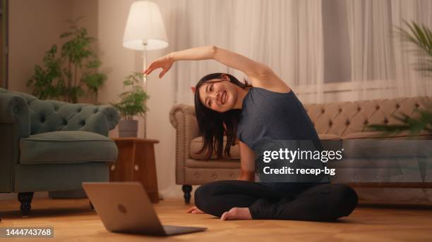 pregnant woman sitting on floor and stretching her body while watching online tutorials on laptop in living room at home - prenatal yoga stock pictures, royalty-free photos & images