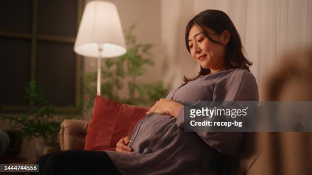 mujer embarazada sentada en el sofá descansando y relajándose en la sala de estar de su casa - night before fotografías e imágenes de stock