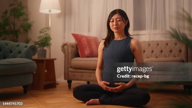 pregnant woman sitting on ground and doing breathing exercises in living room at home - breathing new life stock pictures, royalty-free photos & images