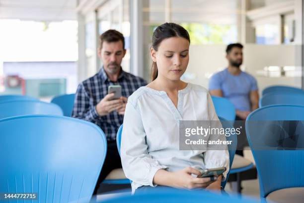 woman in the waiting room at the hospital holding her cell phone - hospital waiting room stockfoto's en -beelden