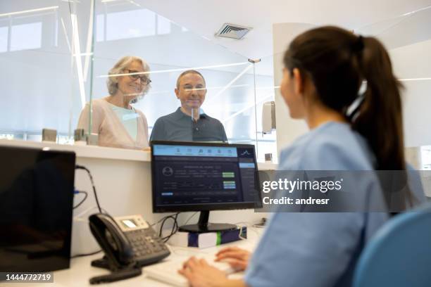 receptionist helping a senior couple registering at the hospital - sekreterare bildbanksfoton och bilder