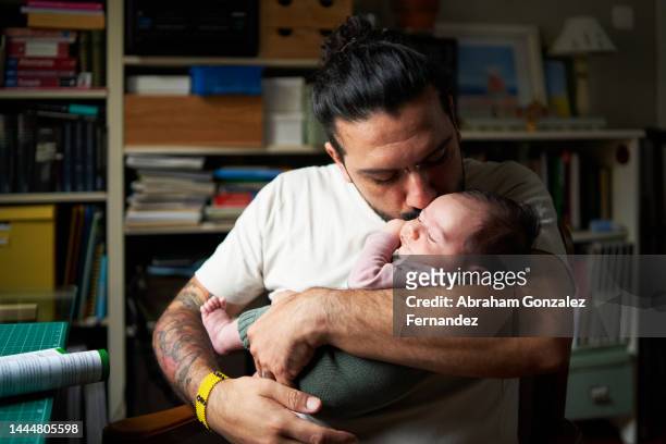 dad kissing his son in arms while sitting indoors - dad and baby stock pictures, royalty-free photos & images