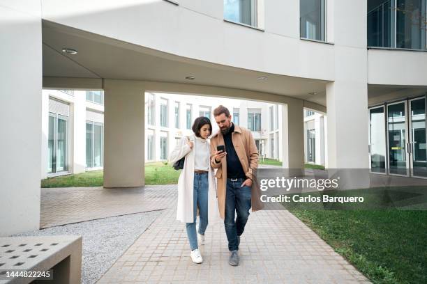 work colleagues walking out of office building using phone to check business topics. - couple full length stock pictures, royalty-free photos & images