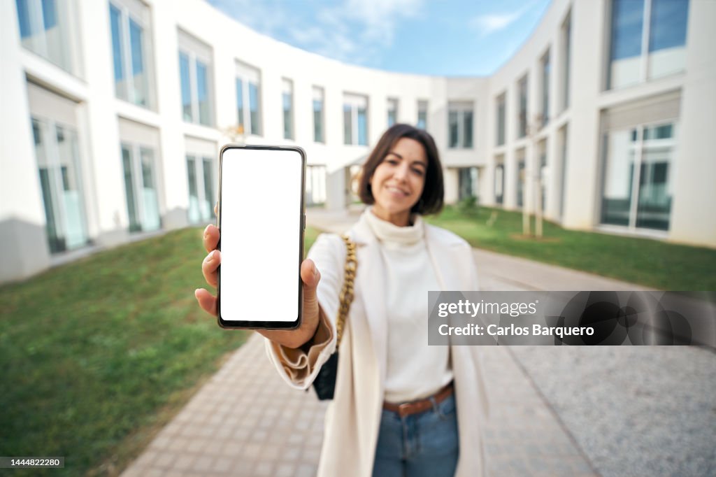 Copy space photo of female doctor showing empty white phone screen standing by a new residential buildings.