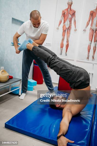 fisioterapeuta ayuda a paciente joven guapo - medicina deportiva fotografías e imágenes de stock