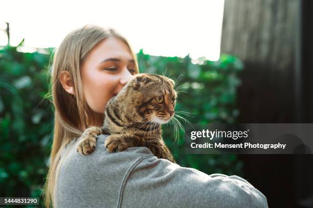 young woman holding in shoulder cat outdoors - tierheim stock-fotos und bilder