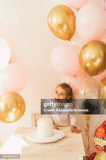 cute little girl blows out candles on a birthday cake at home against a backdrop of balloons. - decorative balloons ストックフォトと画像