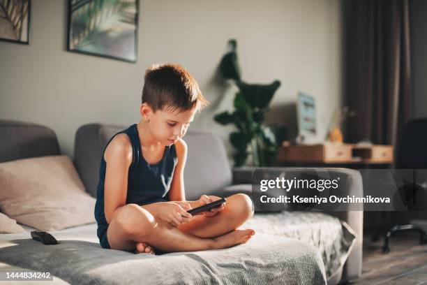 boy playing mobile game on tablet on sofa. preschooler playing mobile games. kid using device for gaming. child playing video game at home. communication and chat device - alleen jongens stockfoto's en -beelden