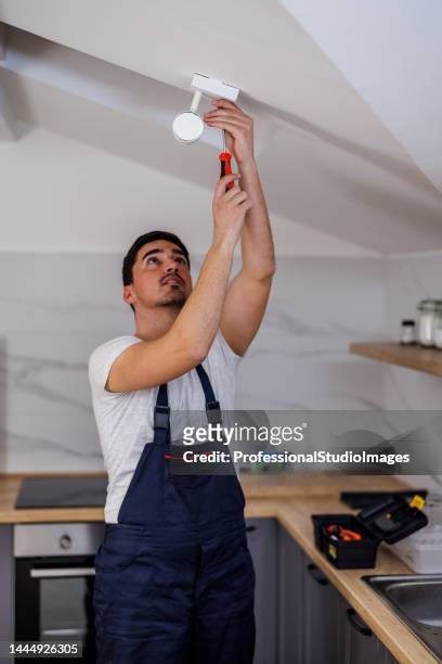 a young maintenance worker is fixing a fire alarm on a ceiling. - broken lamp stockfoto's en -beelden