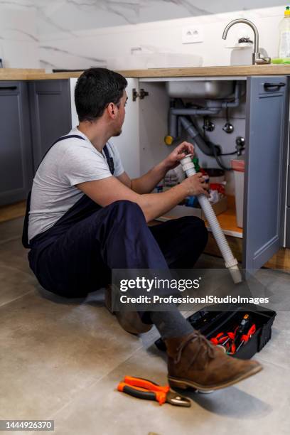 a young worker is repairing a faucet in the kitchen. - looking under sink stock pictures, royalty-free photos & images