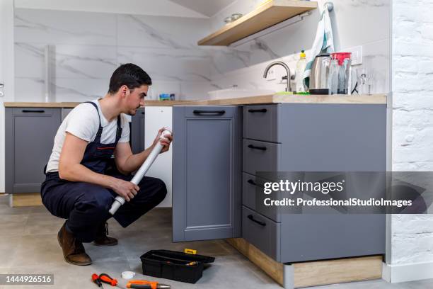 a younger man is working in the kitchen and fixing the faucet. - looking under sink stock pictures, royalty-free photos & images
