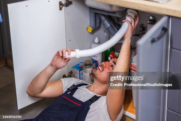 ein junger arbeiter repariert einen wasserhahn in der küche. - drain inspection stock-fotos und bilder