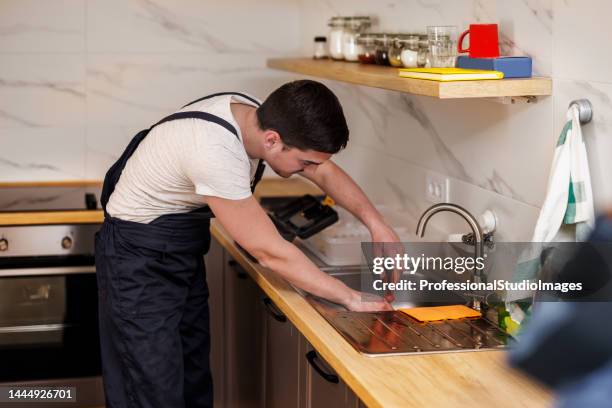 a young worker is repairing a faucet in the kitchen. - looking under sink stock pictures, royalty-free photos & images