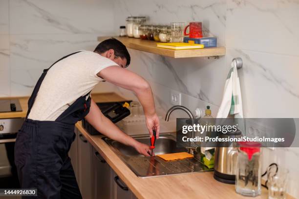 a younger maintenance engineer is working on the kitchen sink. - looking under sink stock pictures, royalty-free photos & images