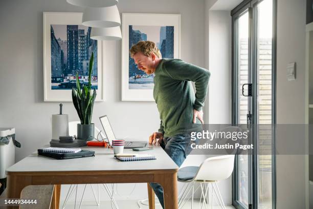 mature man working from home. he suffers from back pain - man working from home stock pictures, royalty-free photos & images