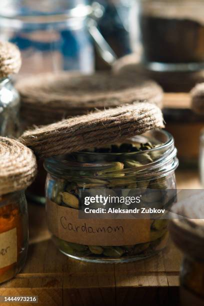 spices and herbs standing in a row on a wooden table or shelf. dried crushed spices and seasonings in glass jars and containers with inscriptions in the kitchen cabinet or pantry, storage of bulk products. the concept of cooking, home decor. - cardamom - fotografias e filmes do acervo