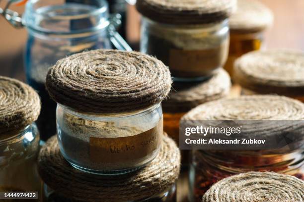 spices and herbs standing in a row on a wooden table or shelf. dried crushed spices and seasonings in glass jars and containers with inscriptions in the kitchen cabinet or pantry, storage of bulk products. the concept of cooking, home decor. - cumin stock-fotos und bilder