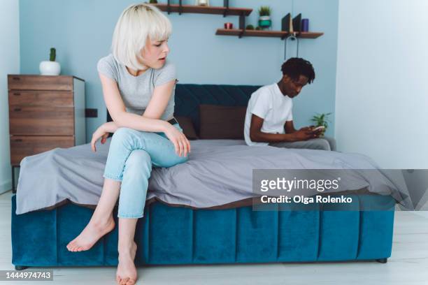 betrayal, cheat on wife. family, couple breaking up. a young international romantic couple sit on a bed in different corners, man using smartphone - relationship difficulties stock pictures, royalty-free photos & images