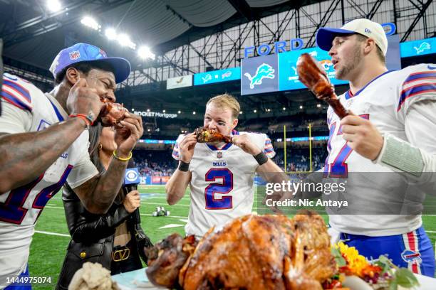 Stefon Diggs, Tyler Bass and Josh Allen of the Buffalo Bills celebrate on the field by eating turkey legs after defeating the Detroit Lions at Ford...