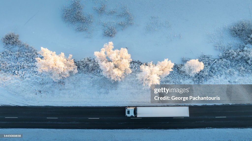 Top down aerial photo of a track on an asphalt road next to a frozen lake covered in snow