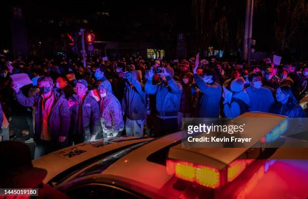 Protesters march by a police cruiser during a protest against Chinas strict zero COVID measures on November 27, 2022 in Beijing, China. Protesters...