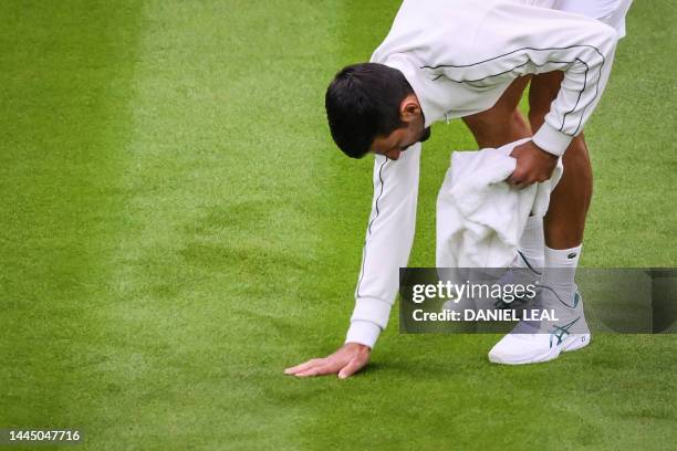 Serbia's Novak Djokovic jokes as he checks the grass of Center Court while attempting to dry it with a towel as the rains starts to fall during his...