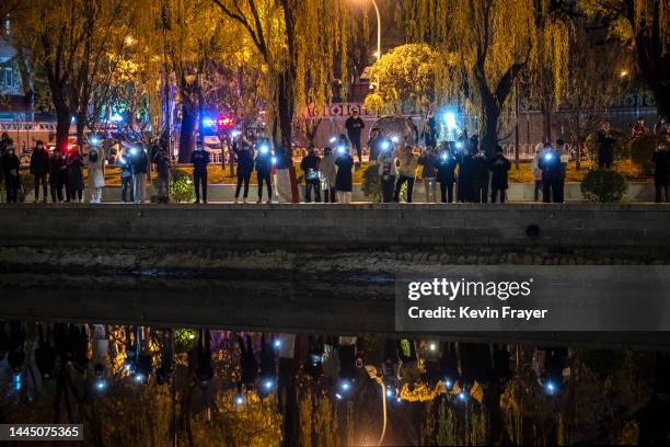 Protesters hold up their mobile phones against China's strict zero COVID measures on the Liangma River on November 27, 2022 in Beijing, China....