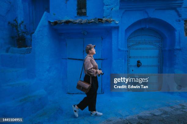 turista asiática china tomando una foto con un teléfono inteligente en el callejón azul de la pared en chefchaouen - arquitectura-islámica fotografías e imágenes de stock