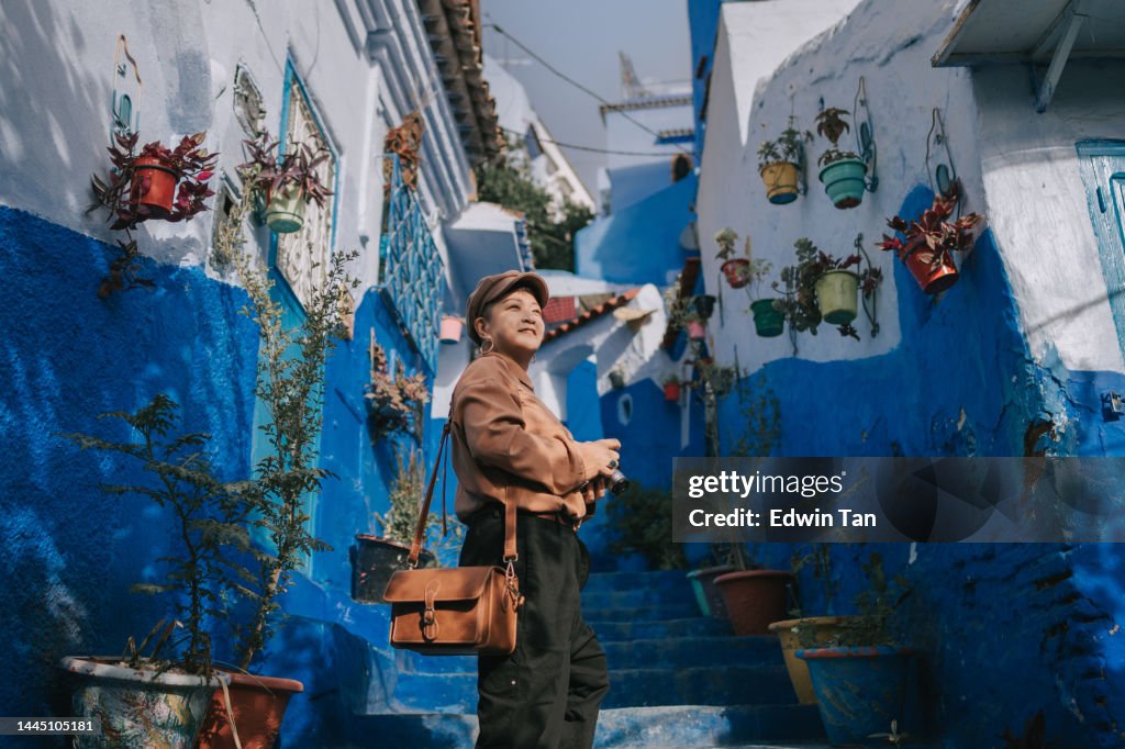 Asiatische chinesische Touristin steht morgens lächelnd in der Gasse in Chefchaouen, Marokko
