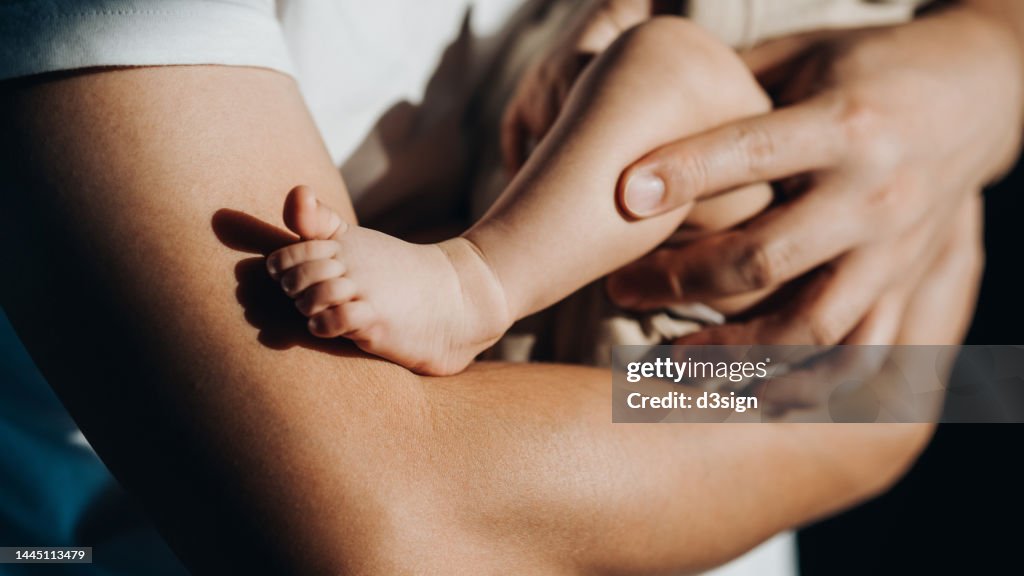 Close up of a loving young Asian father carrying his newborn baby daughter in arms. Bonding moment of father and daughter. Fatherhood. Skin to skin contact. Love, care and tenderness