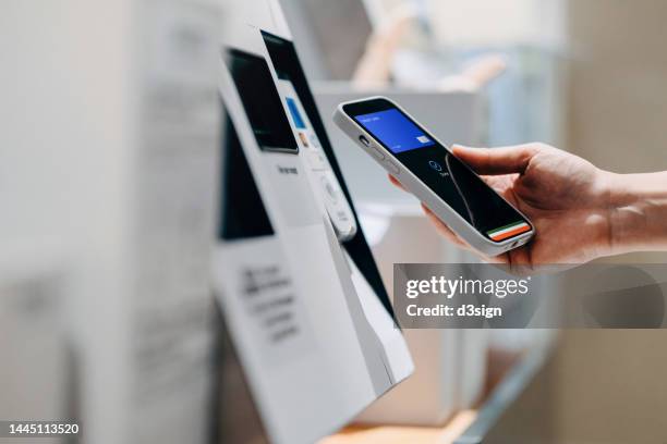 close up of a woman's hand making mobile payment with her smartphone in a shop, scan and pay a bill on a card machine making a quick and easy contactless payment at self checkout counter. nfc technology, tap and go concept - product innovation stock pictures, royalty-free photos & images