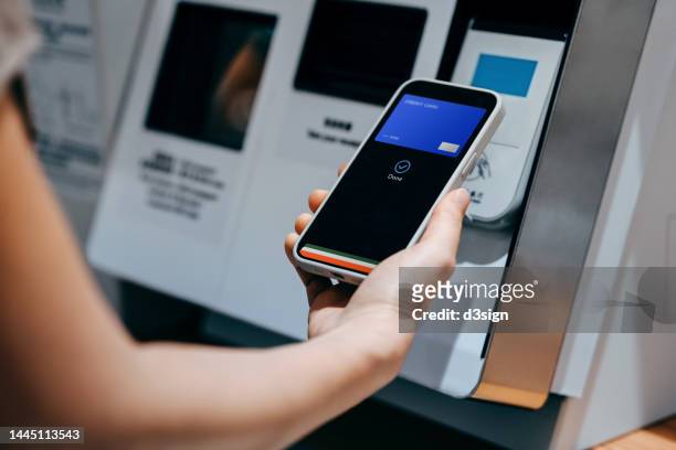 close up of a woman's hand making mobile payment with her smartphone in a shop, scan and pay a bill on a card machine making a quick and easy contactless payment at self checkout counter. nfc technology, tap and go concept - nfc payment stock-fotos und bilder