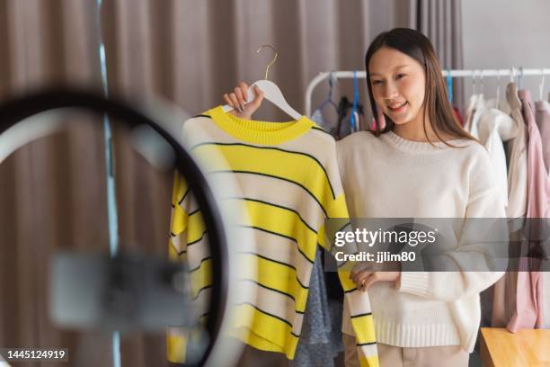 photo of a beautiful young asian female small online business operator doing live broadcast on social media promoting and selling her clothes with promotion discount - online auction stock pictures, royalty-free photos & images